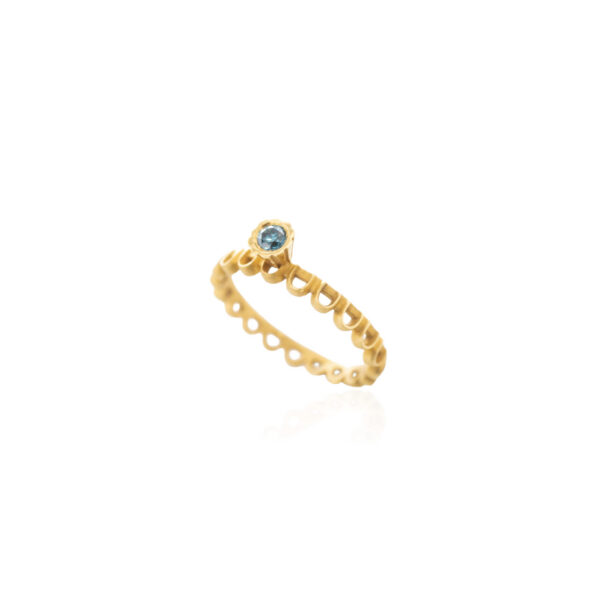 Angled view of the Molyvos engagement ring in 18K yellow gold, featuring a round blue diamond and a band of repeating open semicircles.