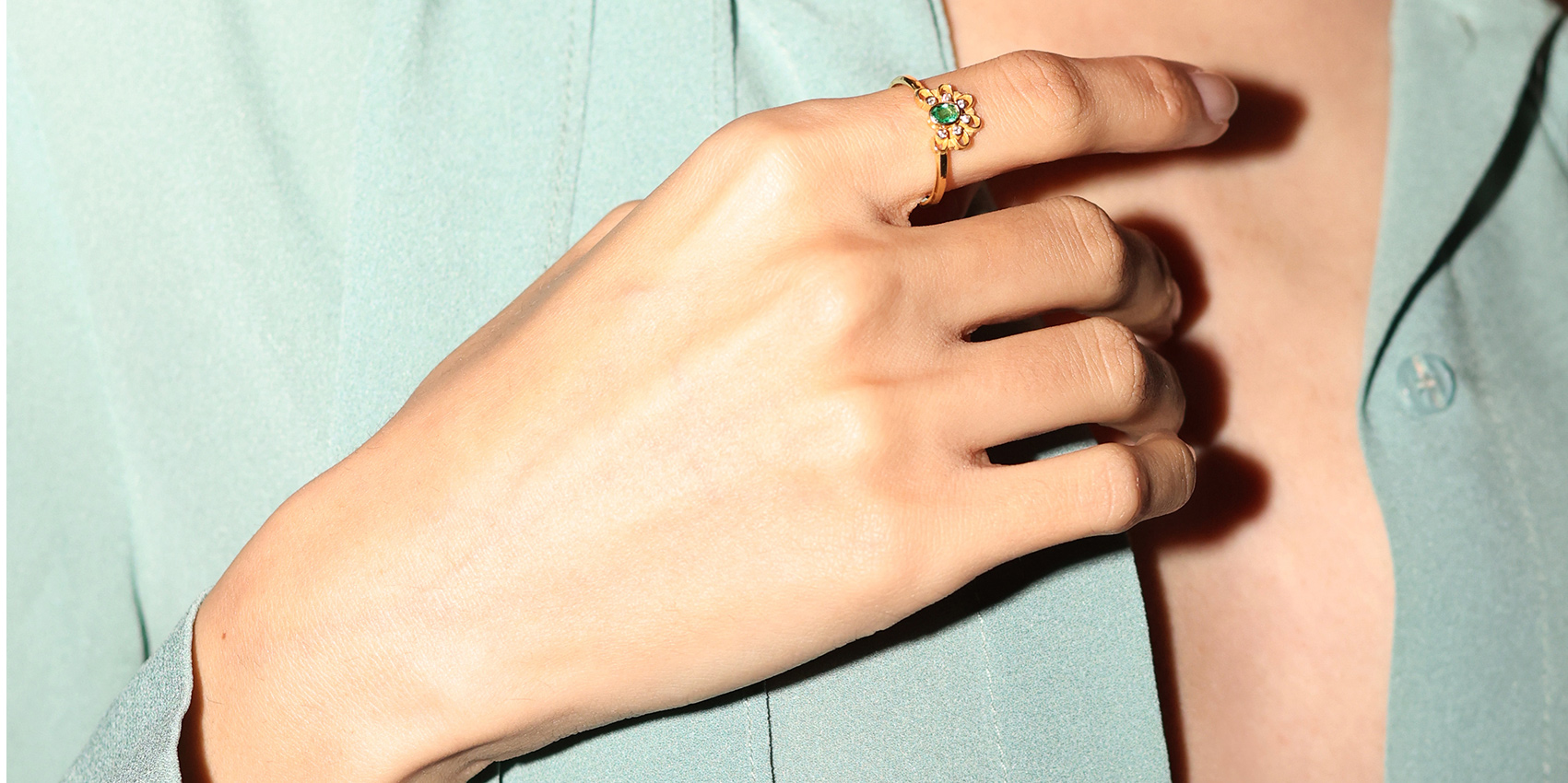 A hand wearing an 18K gold emerald and diamond ring from the Mytilene Fine — Epirroes collection.