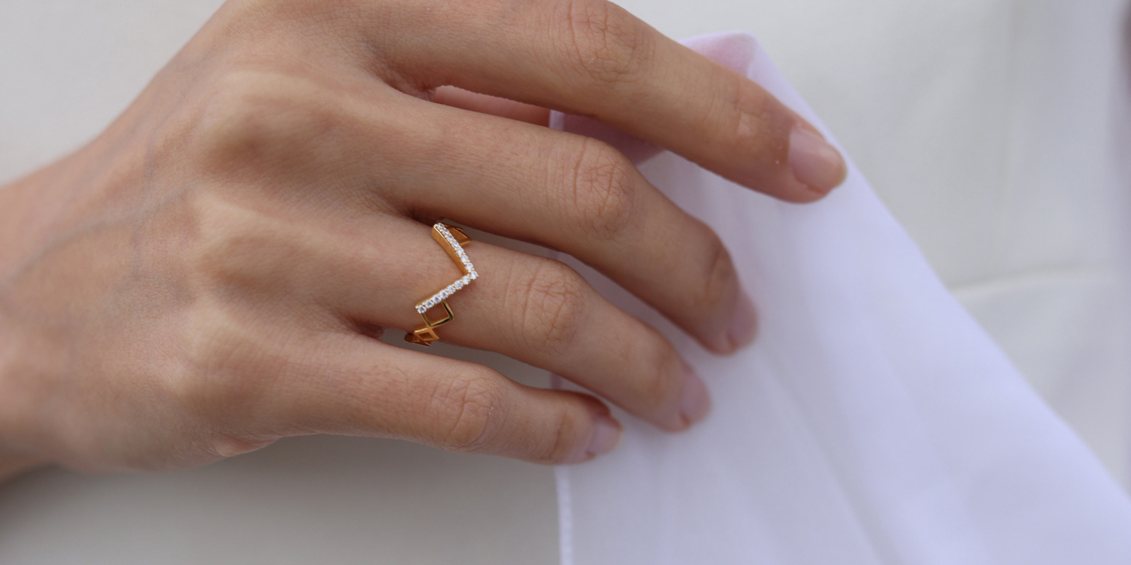 A geometric gold ring with diamonds, worn against white bridal fabric.