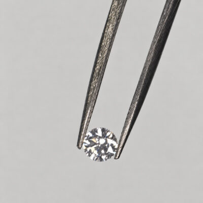 5 mm round brilliant-cut diamond held in jeweller’s tweezers against a soft grey background.