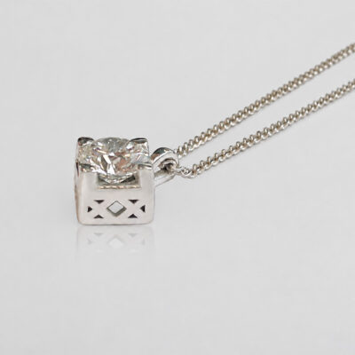 Finished 18k white gold pendant with a 5 mm round brilliant-cut diamond and geometric openwork, on a soft grey background with a subtle reflection.